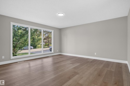 Spacious room featuring a large multi-pane window, wood-finish flooring, white baseboards, and a flush-mount ceiling light fixture - 33 Brookside Avenue, Spruce Grove, AB 