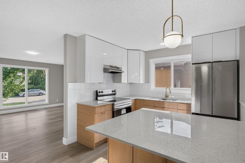 Modern kitchen featuring white upper cabinetry, wood-finish lower cabinetry, and stainless steel appliances - 33 Brookside Avenue, Spruce Grove, AB 