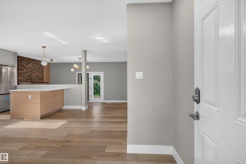Open floor plan featuring wood-finish flooring, a kitchen island with seating, a brick-patterned accent wall, and a stainless steel refrigerator - 33 Brookside Avenue, Spruce Grove, AB 