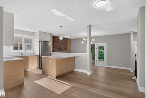 Contemporary kitchen featuring light wood-finish cabinetry, stainless steel appliances, a center island with countertop seating, and wood-finish flooring - 33 Brookside Avenue, Spruce Grove, AB 