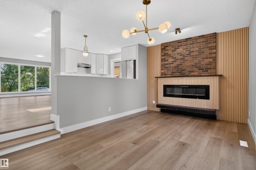 Spacious interior featuring wide plank wood-finish flooring, a modern linear electric fireplace with a brick and wood slat surround, and a contemporary chandelier - 33 Brookside Avenue, Spruce Grove, AB 