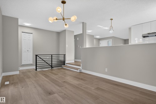 Spacious interior featuring wood-finish flooring, a modern brass chandelier, and a black metal stair railing - 33 Brookside Avenue, Spruce Grove, AB 