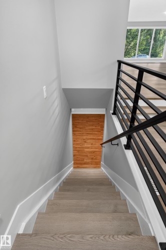 Modern staircase with wood-finish treads, white risers, and a contemporary black metal railing - 33 Brookside Avenue, Spruce Grove, AB 