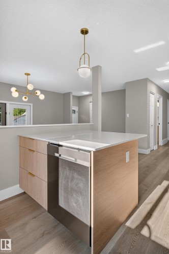 Kitchen island featuring a light wood-finish base, integrated stainless steel dishwasher, and a light-toned countertop - 33 Brookside Avenue, Spruce Grove, AB 