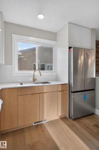 Modern kitchen featuring light wood-finish cabinetry, a stainless steel refrigerator, white subway tile backsplash, and a contemporary gold-finish faucet - 33 Brookside Avenue, Spruce Grove, AB 
