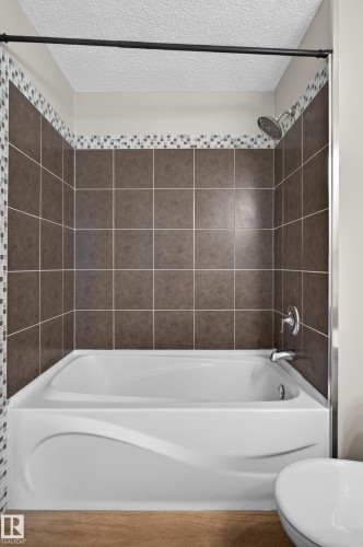 Shower-over-tub combination featuring a white acrylic tub with a curved apron design, brown square wall tiling, a mosaic accent band, and chrome fixtures - 33 Brookside Avenue, Spruce Grove, AB 