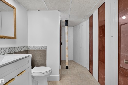 Bathroom vanity featuring a white rectangular sink, wood-framed mirror, and a mosaic tile backsplash - 33 Brookside Avenue, Spruce Grove, AB 