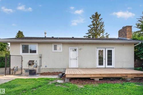 Rear exterior featuring a spacious wood deck, white double French doors, a single white entry door, and a brick chimney - 33 Brookside Avenue, Spruce Grove, AB 