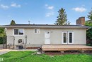 Rear exterior featuring a spacious wood deck, white double French doors, a single white entry door, and a brick chimney - 33 Brookside Avenue, Spruce Grove, AB 