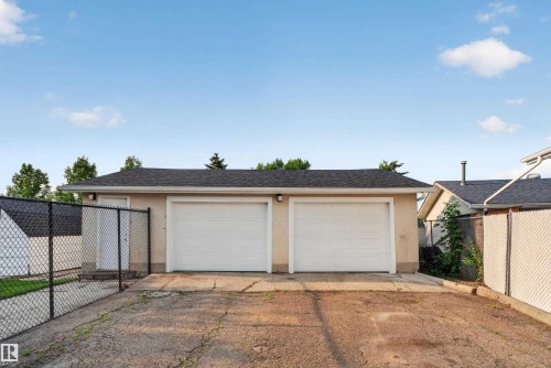 Detached two-car garage with asphalt shingle roofing, beige stucco exterior, and chain-link fencing - 33 Brookside Avenue, Spruce Grove, AB 