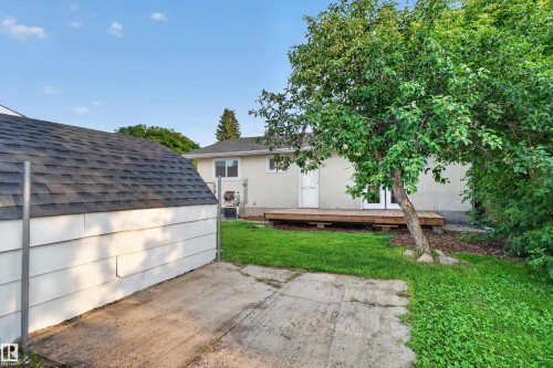 Backyard featuring a wooden deck with double doors, mature trees, a manicured lawn, and a detached shed with shingle roofing - 33 Brookside Avenue, Spruce Grove, AB 