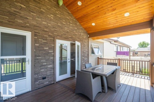 Covered deck featuring a natural wood ceiling, recessed lighting, stone veneer accent wall, and composite decking - 10420 111 Avenue, Westlock, AB 