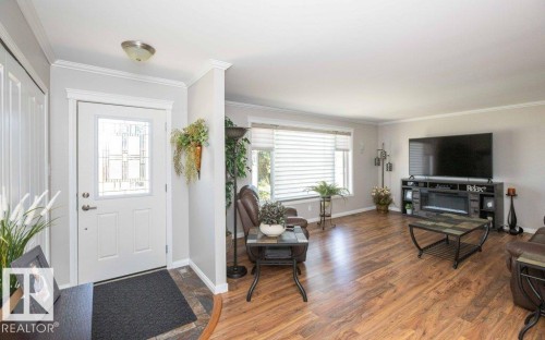 Bright living area featuring wood-finish flooring, an illuminated fireplace insert, and a large window with horizontal blinds - 10420 111 Avenue, Westlock, AB 