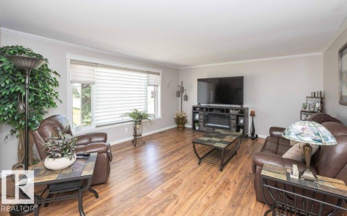 Spacious living area featuring wood-finish flooring, a large picture window with blinds, and white crown molding - 10420 111 Avenue, Westlock, AB 