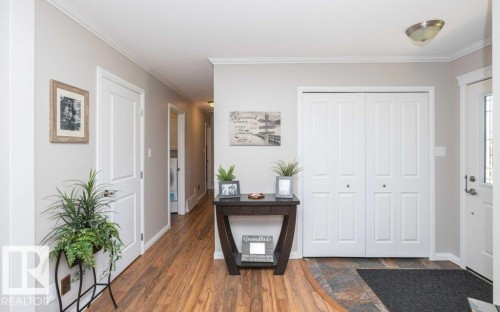 Entryway featuring wood-finish flooring, light grey painted walls, white bi-fold closet doors, a semi-flush mount ceiling light, and crown molding - 10420 111 Avenue, Westlock, AB 