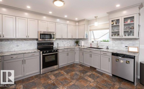 Kitchen featuring gray shaker-style cabinetry, stainless steel appliances, light-toned countertops, a white subway tile backsplash, and multi-toned tile flooring - 10420 111 Avenue, Westlock, AB 