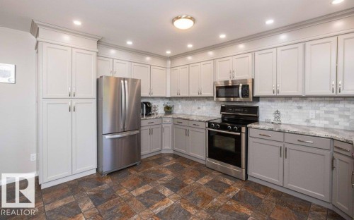 Kitchen featuring light gray cabinetry, stainless steel appliances, speckled countertops, a tile backsplash, and patterned flooring - 10420 111 Avenue, Westlock, AB 