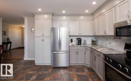 Kitchen featuring light gray shaker cabinetry, stainless steel appliances, speckled stone countertops, a subway tile backsplash, and recessed lighting - 10420 111 Avenue, Westlock, AB 