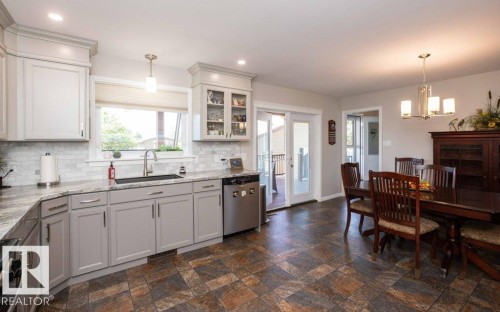 Open-concept kitchen and dining area featuring light-toned cabinetry, a subway tile backsplash, and stone-finish flooring - 10420 111 Avenue, Westlock, AB 
