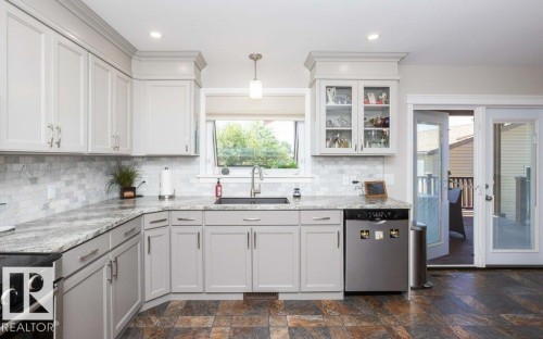 Kitchen featuring a window above the sink, light gray cabinetry, stone countertops, and a full tile backsplash - 10420 111 Avenue, Westlock, AB 