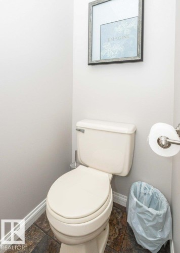 Powder room featuring a ceramic toilet, multi-tone tile flooring, and white baseboards - 10420 111 Avenue, Westlock, AB 