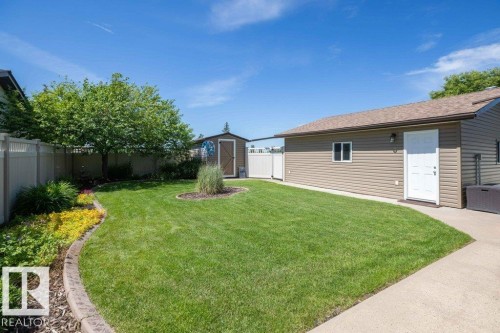 Spacious backyard featuring a manicured lawn, established garden beds with concrete curbing, and a detached storage shed - 10420 111 Avenue, Westlock, AB 