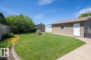 Spacious backyard featuring a manicured lawn, established garden beds with concrete curbing, and a detached storage shed - 10420 111 Avenue, Westlock, AB 
