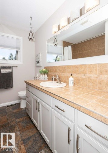 Bathroom featuring a single vanity with white cabinetry, a tiled countertop, and a built-in sink - 10420 111 Avenue, Westlock, AB 