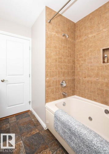 Bathroom featuring a built-in tub with jets, tiled shower surround, recessed shower niche, and multi-toned tile flooring - 10420 111 Avenue, Westlock, AB 