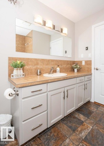 Bathroom vanity featuring an integrated sink, tile countertop, and tile backsplash - 10420 111 Avenue, Westlock, AB 