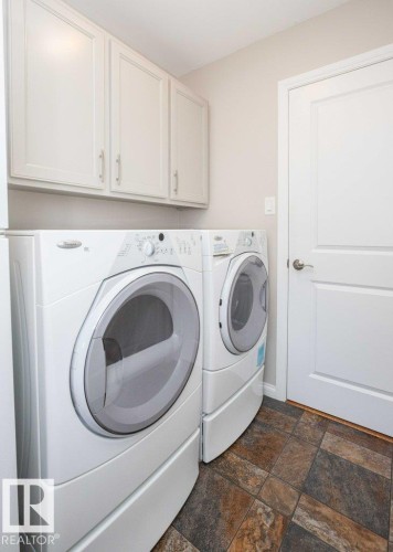 Laundry space featuring upper cabinetry, multi-toned tile flooring, and a paneled door - 10420 111 Avenue, Westlock, AB 