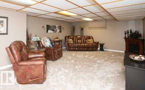 Spacious recreational room featuring light-toned patterned carpeting and a drop ceiling with recessed lighting - 10420 111 Avenue, Westlock, AB 