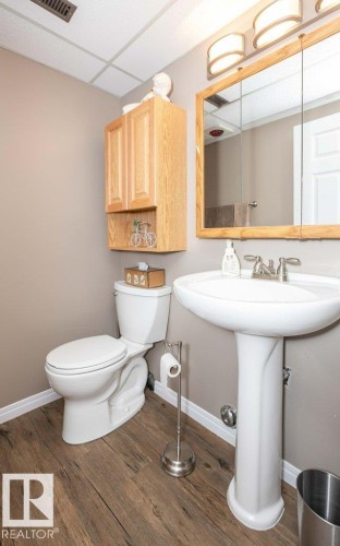 Bathroom featuring wood-finish flooring, a white pedestal sink, a wood-framed mirrored medicine cabinet, and a natural wood wall cabinet - 10420 111 Avenue, Westlock, AB 