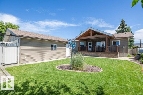 Expansive backyard featuring a manicured lawn, landscaping, and a covered porch - 10420 111 Avenue, Westlock, AB 