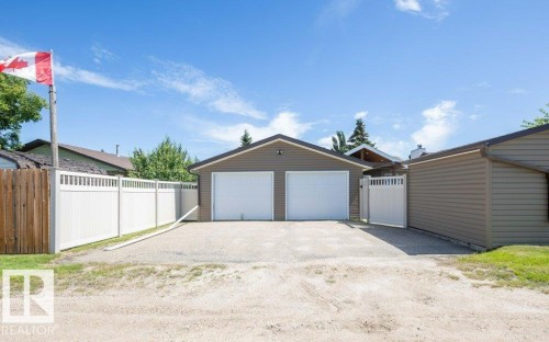 Detached double garage with tan siding, twin white garage doors, and a gravel driveway - 10420 111 Avenue, Westlock, AB 