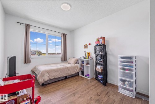 Spacious room featuring wood-finish flooring, a large multi-pane window, and white walls - 16 19904 31 Avenue, Edmonton, AB 