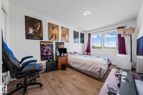 Bedroom featuring wood-finish flooring, a window with exterior scenery, white painted walls, and a ceiling-mounted light fixture - 16 19904 31 Avenue, Edmonton, AB 