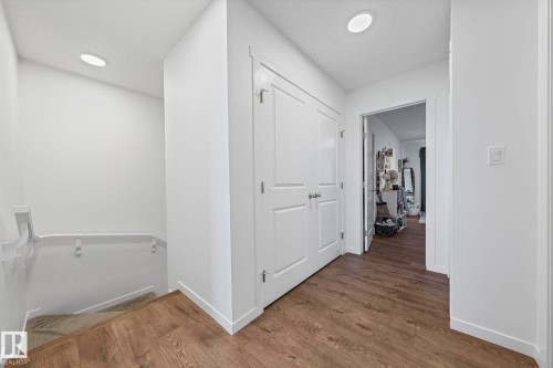 Hallway featuring wood-finish flooring, recessed lighting, white trim, and a white paneled door - 16 19904 31 Avenue, Edmonton, AB 