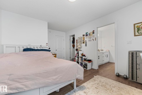 Bedroom featuring wood-finish flooring, white walls, and an attached bathroom with a single vanity and white cabinetry - 16 19904 31 Avenue, Edmonton, AB 