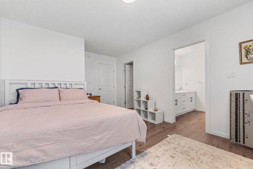 Spacious bedroom featuring wood-finish flooring and a white headboard - 16 19904 31 Avenue, Edmonton, AB 