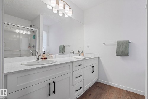 Double vanity with white cabinetry and dark hardware, featuring dual integrated sinks - 16 19904 31 Avenue, Edmonton, AB 