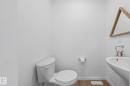 Contemporary powder room featuring a wall-mounted sink, white toilet, wood-finish flooring, and white baseboards - 16 19904 31 Avenue, Edmonton, AB 
