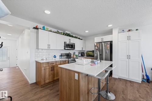 Well-appointed kitchen featuring white upper cabinetry, wood-finish lower cabinetry, and a white subway tile backsplash - 16 19904 31 Avenue, Edmonton, AB 