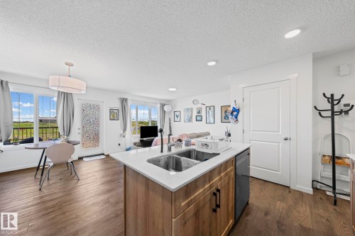 Open-concept kitchen and living area featuring wood-finish flooring, a kitchen island with dual sinks and light-toned countertop, and recessed lighting - 16 19904 31 Avenue, Edmonton, AB 