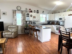 Open-concept living space featuring wood-finish flooring, a vaulted ceiling, and a kitchen with white cabinetry - 
