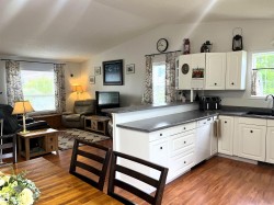 Open-concept living space featuring a kitchen with white cabinetry and dark countertops, a breakfast bar, and wood-finish flooring - 