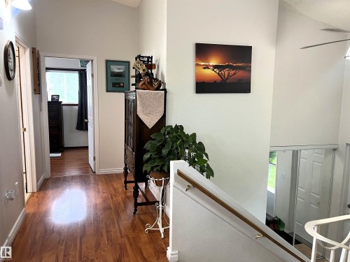 Hallway with wood-finish flooring extending into a room with a window, featuring a vaulted ceiling and a staircase with a wooden handrail - 4914 51 Ave, Entwistle, AB 