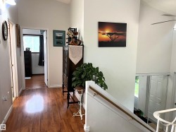 Hallway with wood-finish flooring extending into a room with a window, featuring a vaulted ceiling and a staircase with a wooden handrail - 