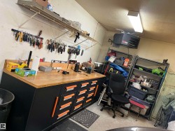 Functional workshop area featuring a large wood-finish countertop workbench with built-in storage drawers, overhead fluorescent lighting, wall-mounted shelving, and organizational tool racks - 