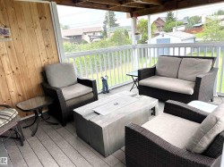 Covered outdoor deck featuring composite decking, wood-paneled wall, white railings, and a concrete fire pit - 
